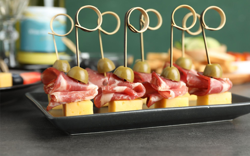 Aperitivos fríos de jamón, queso y aceitunas servidos en brochetas para una celebración