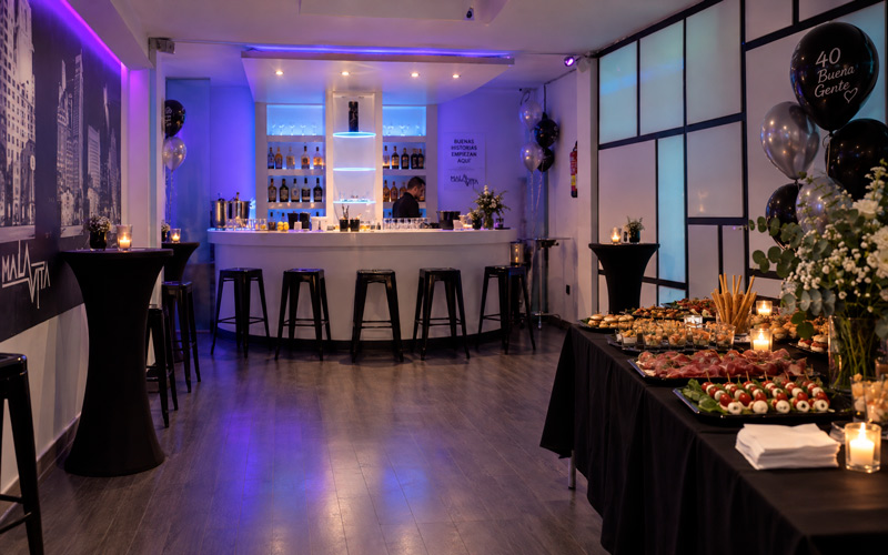Sala privada preparada para una fiesta para 50 personas, con barra, mesas altas y catering